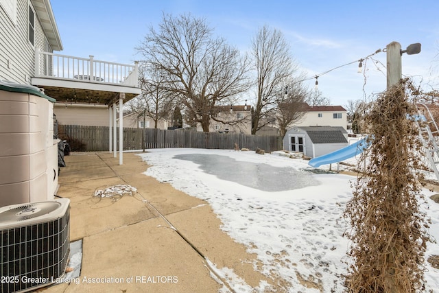 snowy yard with cooling unit, a storage shed, and a balcony