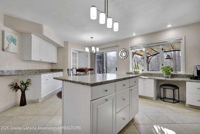 kitchen featuring light tile patterned floors, stone counters, white cabinetry, a kitchen island, and decorative light fixtures