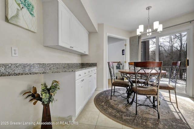 kitchen with an inviting chandelier, hanging light fixtures, light tile patterned floors, light stone countertops, and white cabinets