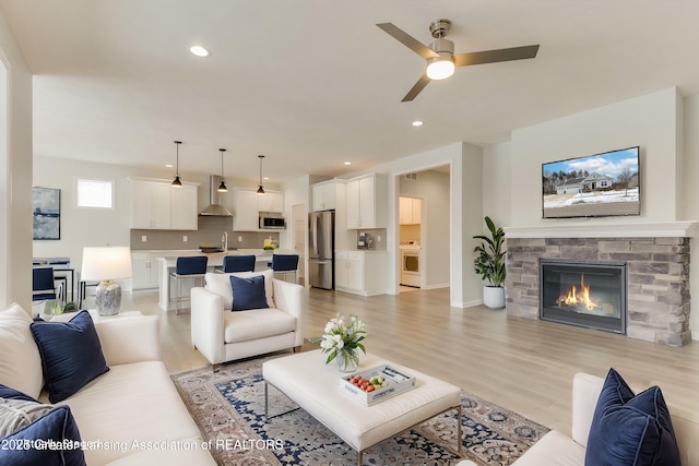 living room with ceiling fan, a stone fireplace, and light hardwood / wood-style floors