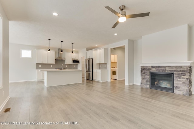 unfurnished living room with a stone fireplace, sink, light hardwood / wood-style flooring, ceiling fan, and washer / clothes dryer