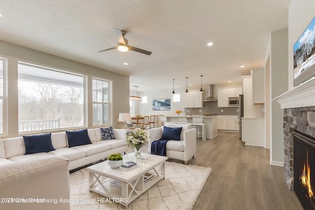 living room featuring ceiling fan, a stone fireplace, and light wood-type flooring