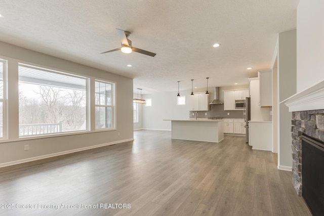 unfurnished living room with wood-type flooring, a textured ceiling, ceiling fan, and a fireplace