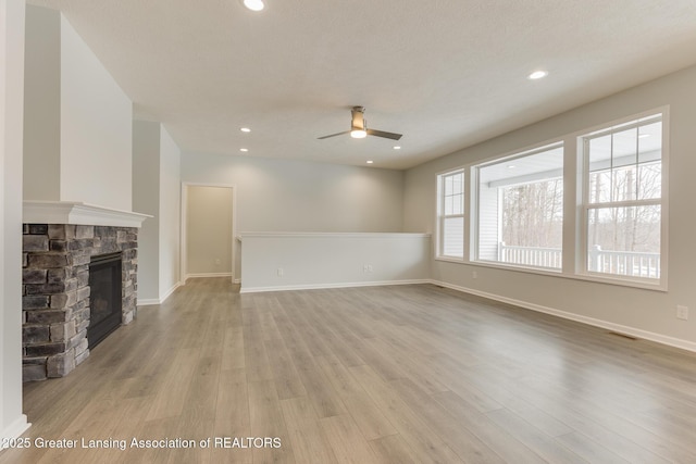 unfurnished living room with a stone fireplace, light hardwood / wood-style floors, ceiling fan, and a textured ceiling