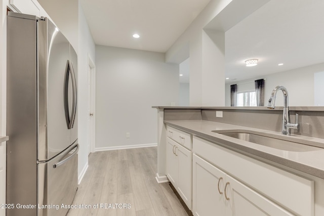 kitchen featuring sink, white cabinets, stainless steel refrigerator, and light hardwood / wood-style flooring