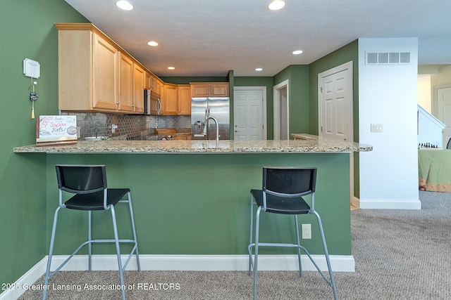 kitchen with appliances with stainless steel finishes, backsplash, a kitchen breakfast bar, light colored carpet, and kitchen peninsula