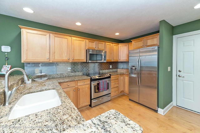 kitchen with tasteful backsplash, sink, stainless steel appliances, light stone countertops, and light wood-type flooring