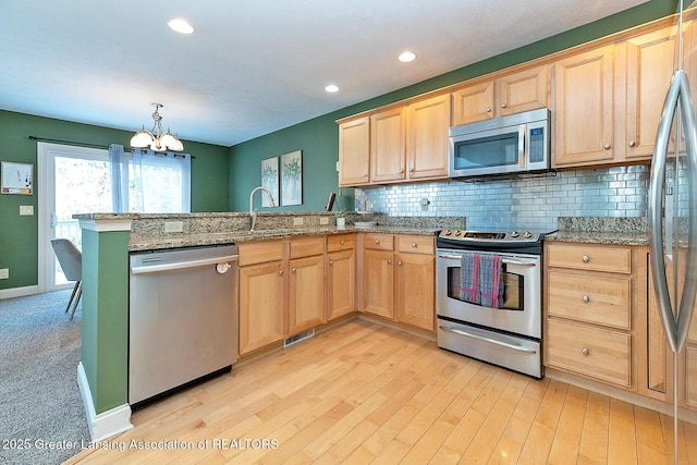 kitchen with sink, appliances with stainless steel finishes, kitchen peninsula, light stone countertops, and decorative backsplash