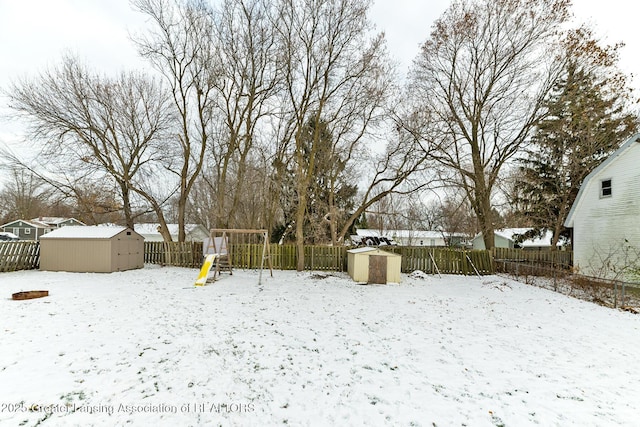 yard covered in snow featuring a playground and a storage shed