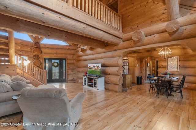 living room featuring a high ceiling, rustic walls, a notable chandelier, and light wood-type flooring