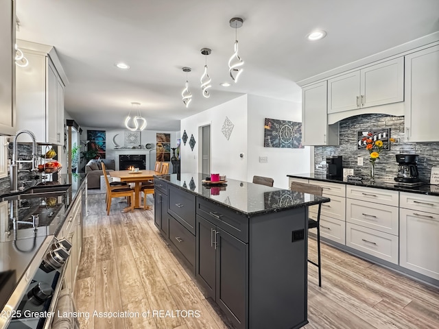 kitchen featuring a breakfast bar area, hanging light fixtures, a center island, tasteful backsplash, and dark stone counters