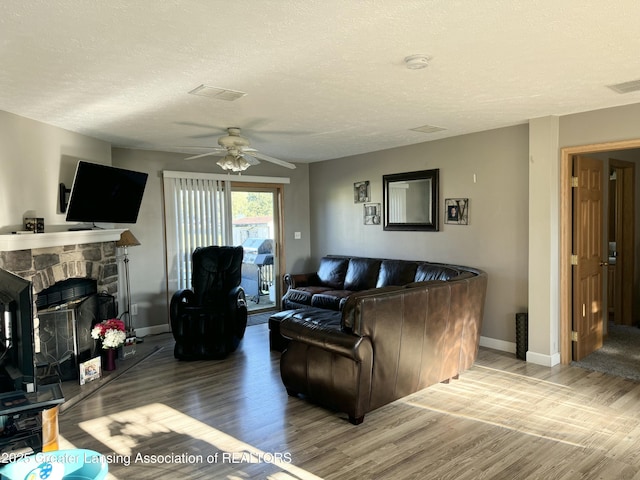 living room featuring hardwood / wood-style flooring, ceiling fan, a textured ceiling, and a fireplace