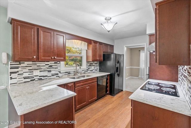 kitchen featuring light wood finished floors, a peninsula, a sink, black appliances, and tasteful backsplash