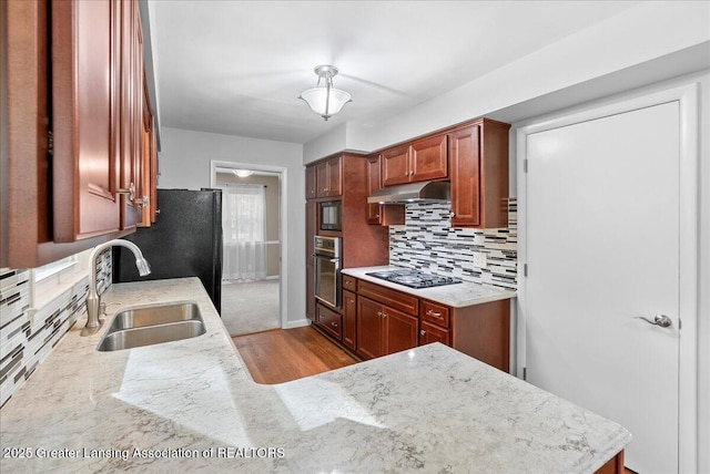 kitchen with oven, under cabinet range hood, light stone counters, a sink, and stovetop