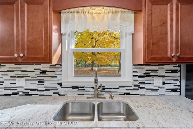 kitchen featuring a sink, decorative backsplash, light stone counters, and plenty of natural light