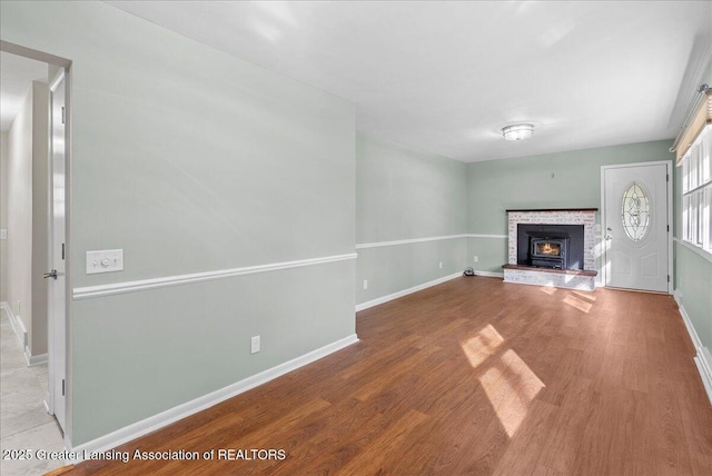 unfurnished living room featuring baseboards, a warm lit fireplace, and wood finished floors