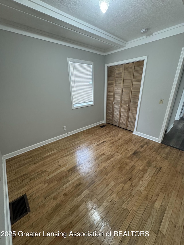 unfurnished bedroom featuring crown molding, a closet, hardwood / wood-style floors, and a textured ceiling