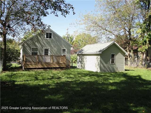 rear view of house featuring an outdoor structure, a deck, and a lawn