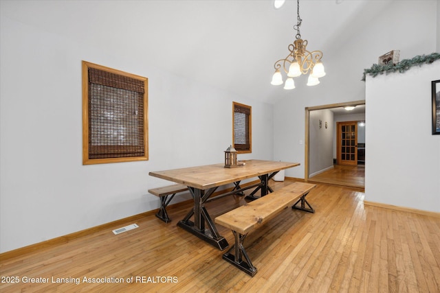 dining space with lofted ceiling, a notable chandelier, and light wood-type flooring