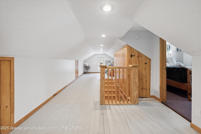 additional living space featuring vaulted ceiling, a textured ceiling, and light wood-type flooring