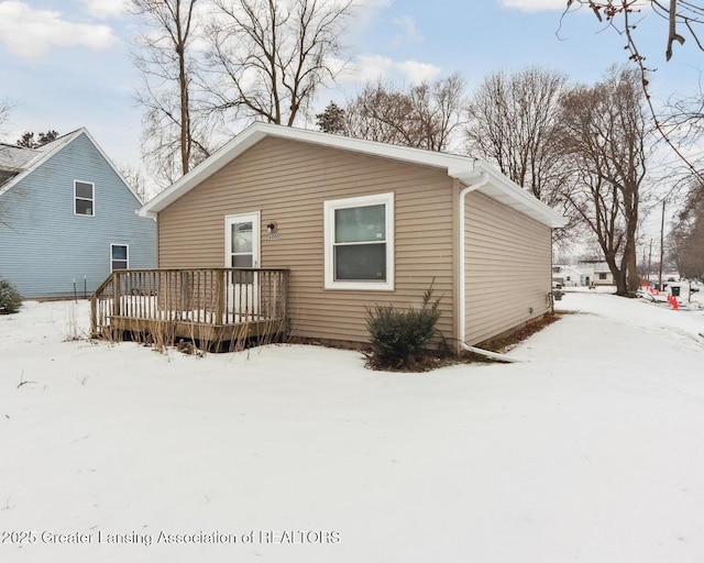 snow covered back of property with a wooden deck