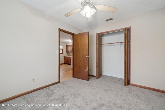 unfurnished bedroom with light carpet, a textured ceiling, a closet, and ceiling fan