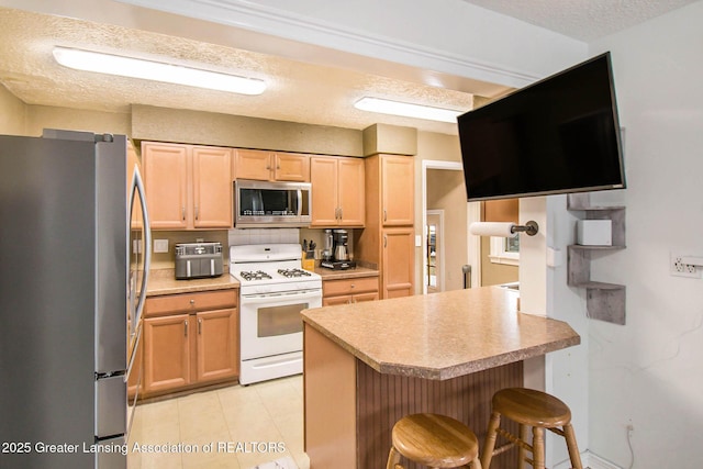 kitchen with appliances with stainless steel finishes, a kitchen breakfast bar, kitchen peninsula, light brown cabinets, and a textured ceiling