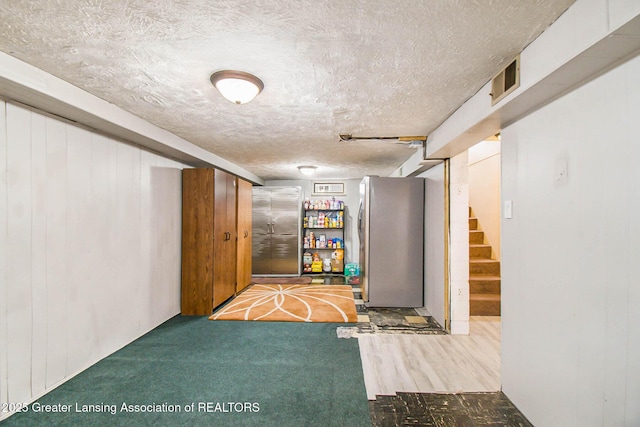 basement featuring wooden walls, stainless steel fridge, carpet, and a textured ceiling