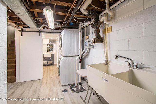 laundry area with stacked washing maching and dryer, sink, and light hardwood / wood-style flooring