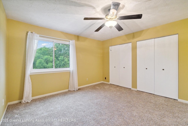 unfurnished bedroom with ceiling fan, carpet flooring, two closets, and a textured ceiling