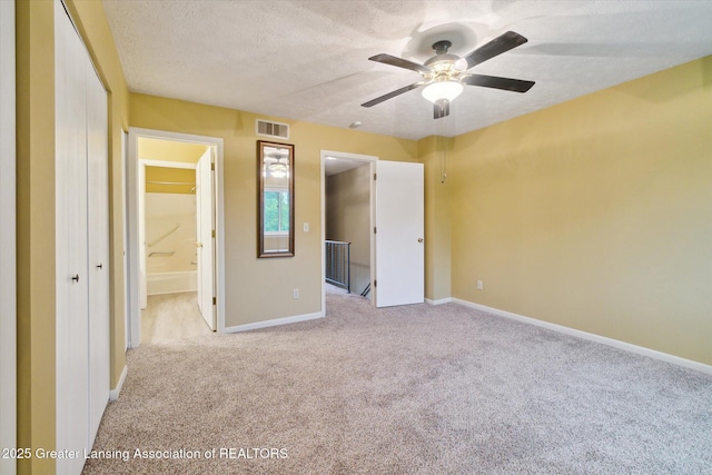 unfurnished bedroom featuring ensuite bathroom, light colored carpet, ceiling fan, and a textured ceiling