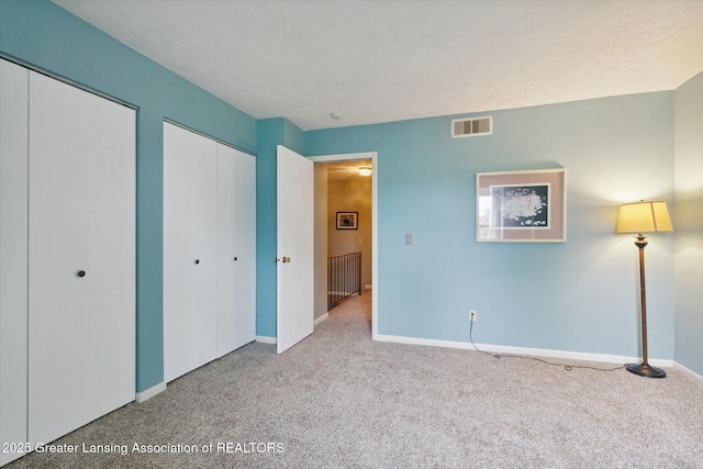 unfurnished bedroom featuring multiple closets, light carpet, and a textured ceiling