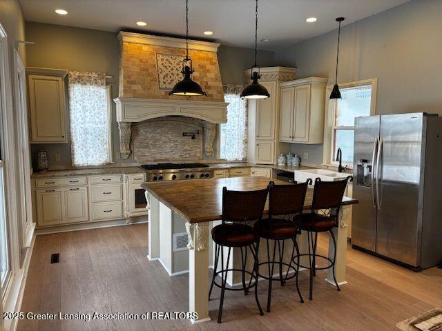 kitchen featuring cream cabinets, a center island, stainless steel fridge with ice dispenser, and hanging light fixtures