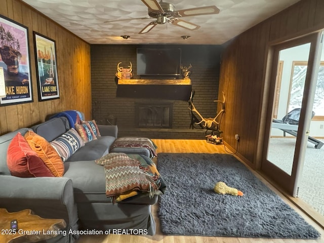 living room featuring ceiling fan, light hardwood / wood-style floors, a brick fireplace, and wood walls