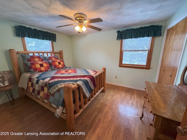 bedroom with multiple windows, wood-type flooring, a closet, and ceiling fan