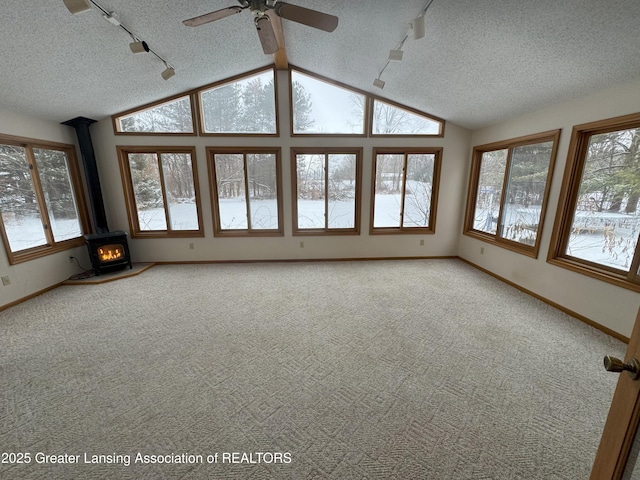 unfurnished sunroom featuring track lighting, plenty of natural light, vaulted ceiling, and a wood stove