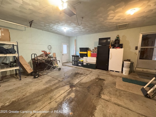 garage with white refrigerator, black refrigerator, and a garage door opener