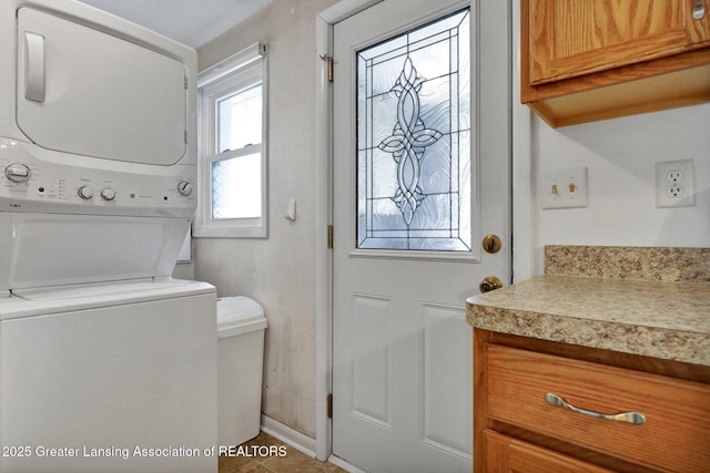 clothes washing area with stacked washer and dryer and cabinets