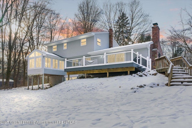 snow covered back of property featuring a deck and a sunroom