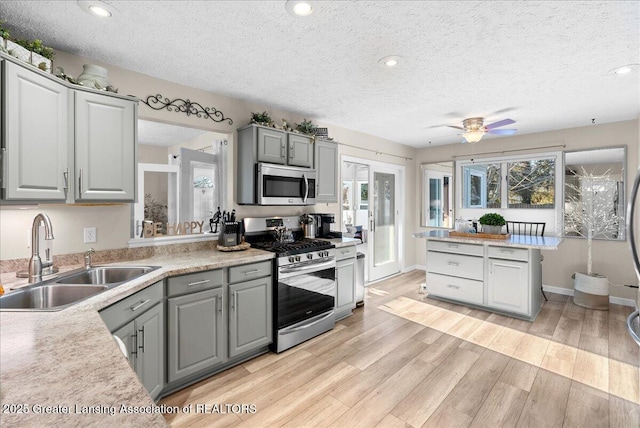 kitchen with appliances with stainless steel finishes, sink, gray cabinetry, light wood-type flooring, and a textured ceiling