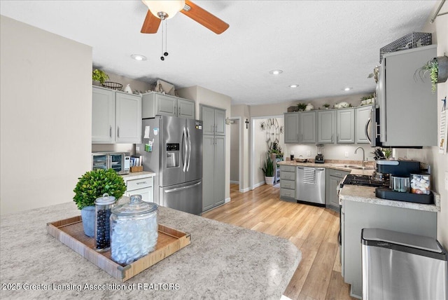 kitchen with appliances with stainless steel finishes, gray cabinetry, a textured ceiling, and light hardwood / wood-style floors