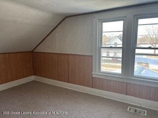 bonus room with vaulted ceiling and wood walls