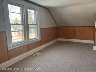 additional living space with lofted ceiling, wooden walls, and carpet flooring