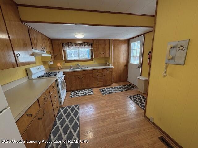 kitchen featuring wooden walls, white range with gas cooktop, sink, and light hardwood / wood-style floors