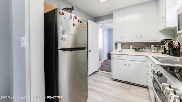 kitchen featuring sink, white cabinetry, light hardwood / wood-style flooring, stainless steel appliances, and backsplash