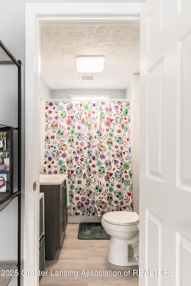 bathroom with vanity, wood-type flooring, a textured ceiling, a shower with curtain, and toilet