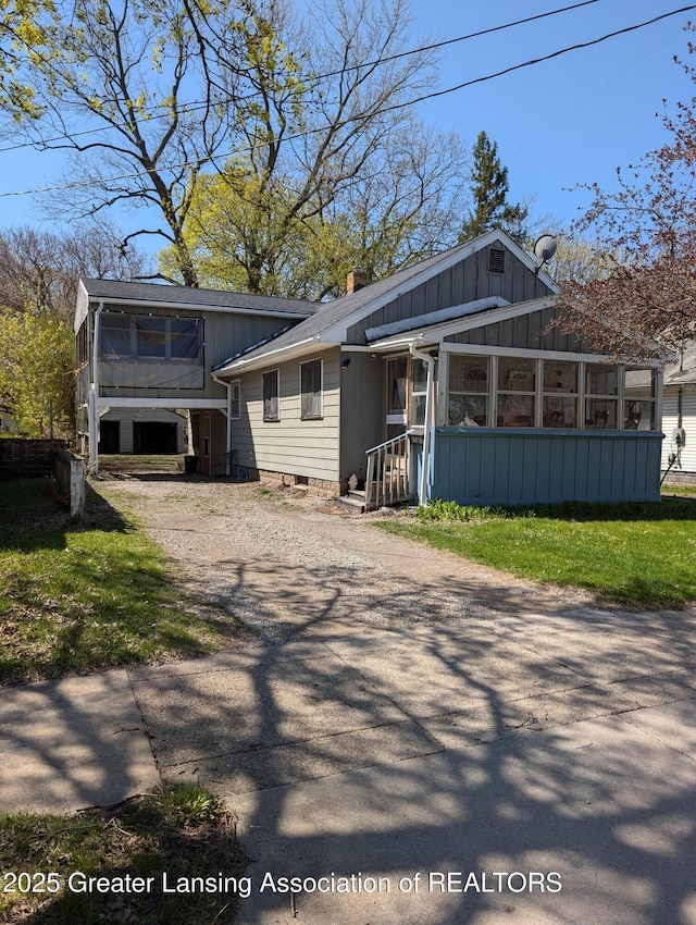 411 Filley St, Lansing, MI 48906 - view of front of house with board and batten siding, a sunroom, a chimney, and driveway