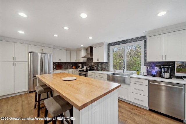 kitchen with a kitchen island, white cabinetry, a kitchen bar, stainless steel appliances, and wall chimney exhaust hood