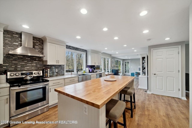 kitchen with wall chimney range hood, sink, appliances with stainless steel finishes, white cabinets, and a kitchen island