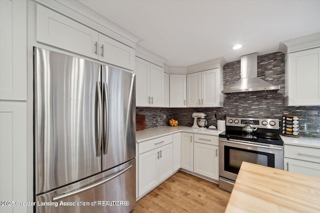 kitchen featuring appliances with stainless steel finishes, light hardwood / wood-style floors, white cabinets, decorative backsplash, and wall chimney exhaust hood